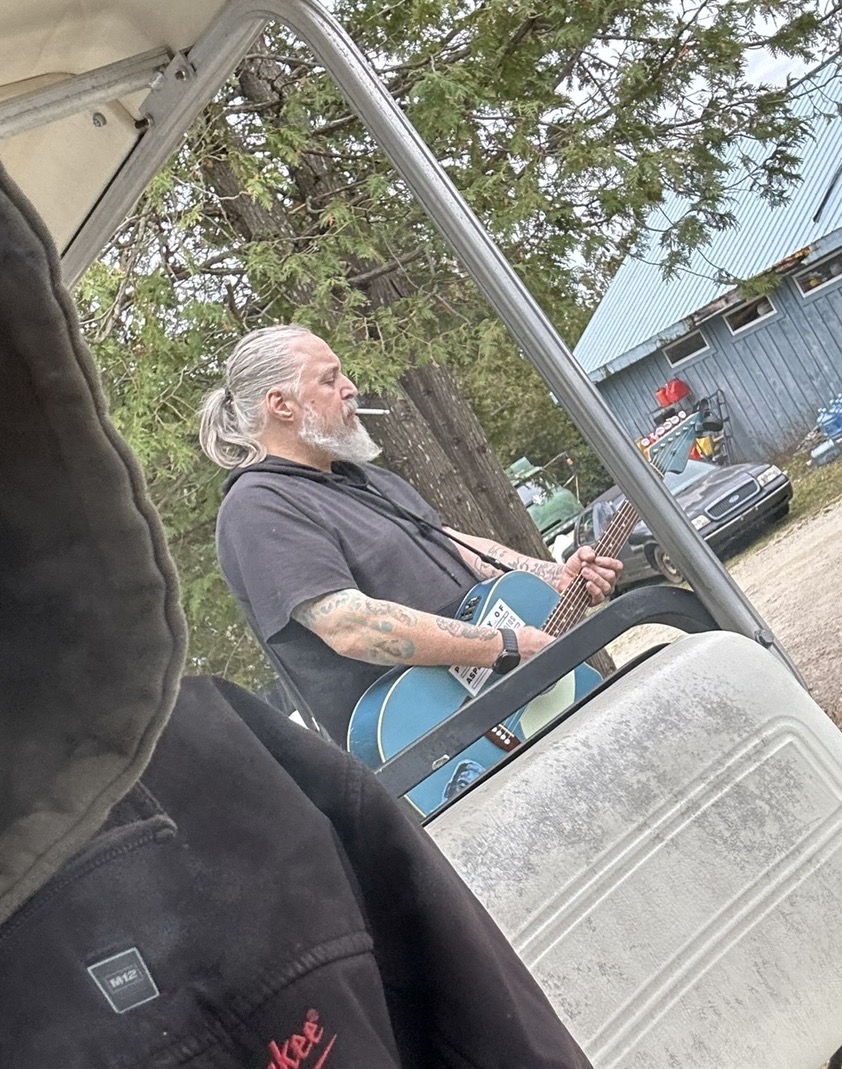Billy da Kid playing a blue acoustic guitar beside his van